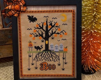 Puede incluir: Un diseño de punto de cruz enmarcado que presenta un árbol de Halloween espeluznante con calabazas naranjas, un gato negro y tres fantasmas. El árbol tiene una luz brillante en el tronco y las palabras "Boo" están bordadas en la parte inferior.