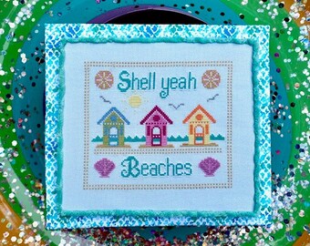 May include: A cross-stitch design featuring three beach houses, a sun, two seashells, and the text "Shell yeah Beaches". The design is framed with a blue and white patterned border.
