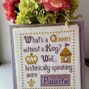 May include: A purple and gold cross-stitch embroidery on a white background with the text "What's a Queen without a King? Well... historically speaking more Powerful".