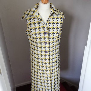 May include: A sleeveless dress with a yellow, white and black houndstooth pattern. The dress has a collar and a button-up front.