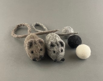 May include: Two felt mice toys with long tails, one gray and one brown, with three felt balls in the background: one gray, one black, and one white.