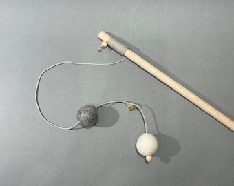 May include: A wooden stick with a string attached to two felt balls, one gray and one white. The string is attached to the stick with a small wooden bead.