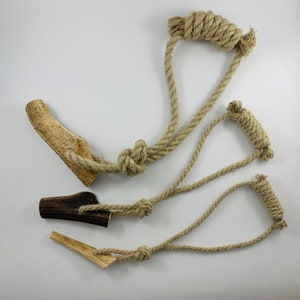 以下が含まれることがあります： 天然の鹿の角とロープで作られた犬用噛み玩具3個セット。鹿の角の部分は茶色で、自然なざらざらした質感です。ロープはベージュで、さまざまな形に結ばれています。