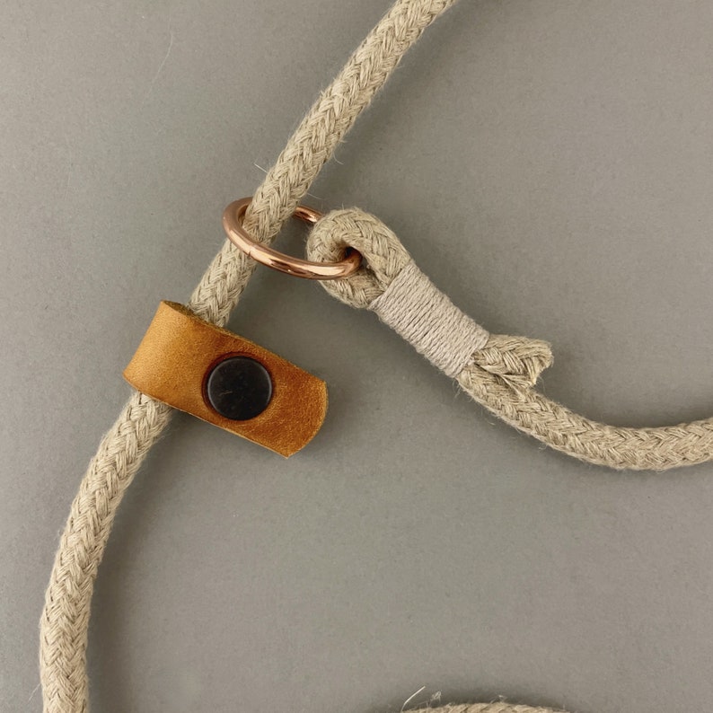 May include: A beige rope dog leash with a brown leather handle and a rose gold metal ring.