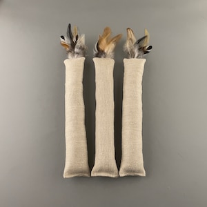May include: Three beige catnip toys with different colored feathers on top. The toys are made of a soft, natural fabric.