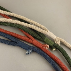May include: A close-up of five different colored cords, including beige, green, red, and blue. The cords are woven together and appear to be made of natural fibers.