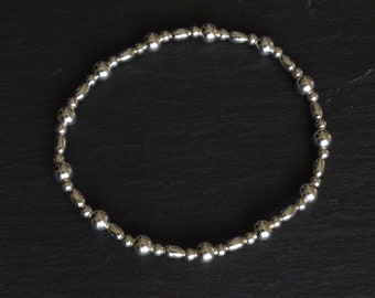 Puede incluir: Un brazalete de plata con un diseño sencillo. El brazalete está hecho de pequeñas cuentas redondas que están conectadas por una fina cadena de plata.