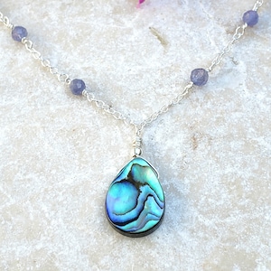 May include: A silver chain necklace with a teardrop-shaped abalone shell pendant and small amethyst beads.