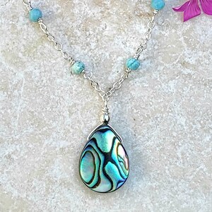 May include: A silver chain necklace with turquoise beads and a teardrop-shaped abalone shell pendant.