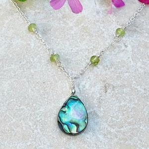 May include: A silver chain necklace with green gemstone beads and a teardrop-shaped abalone shell pendant.