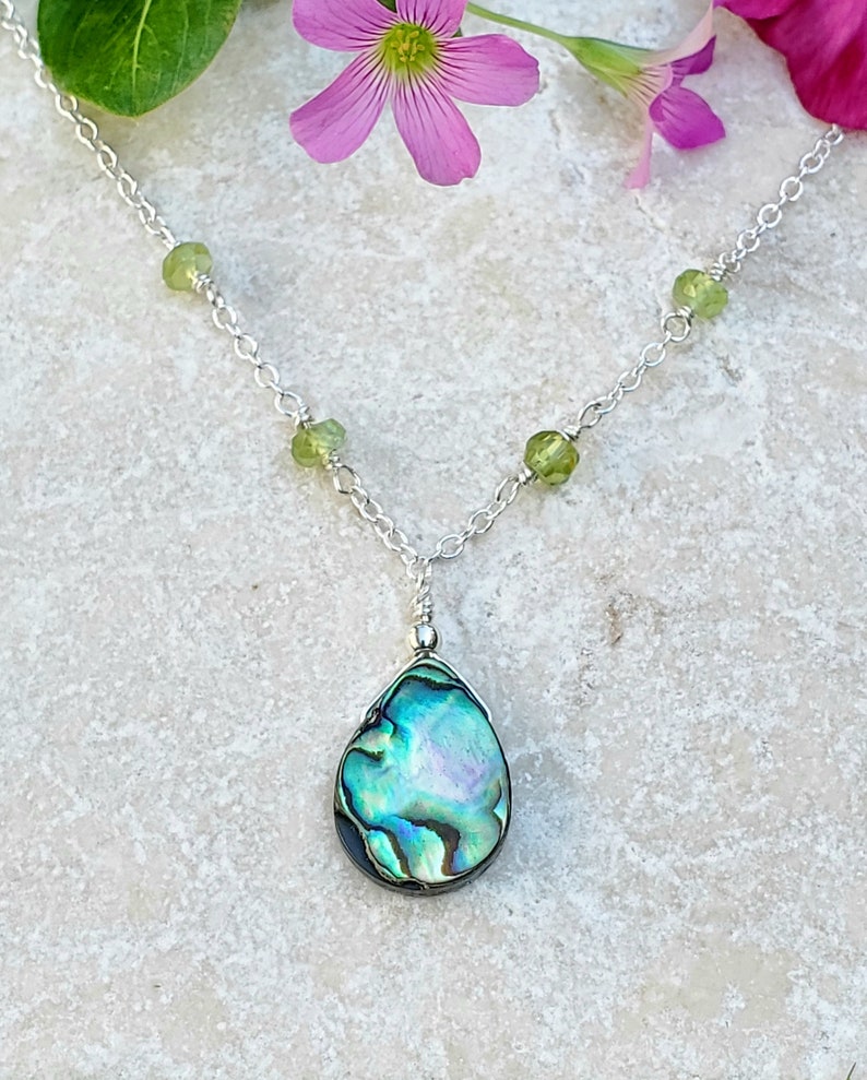 May include: A silver chain necklace with green gemstone beads and a teardrop-shaped abalone shell pendant.