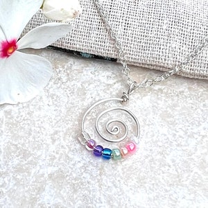 May include: A silver necklace with a spiral charm and rainbow colored beads.