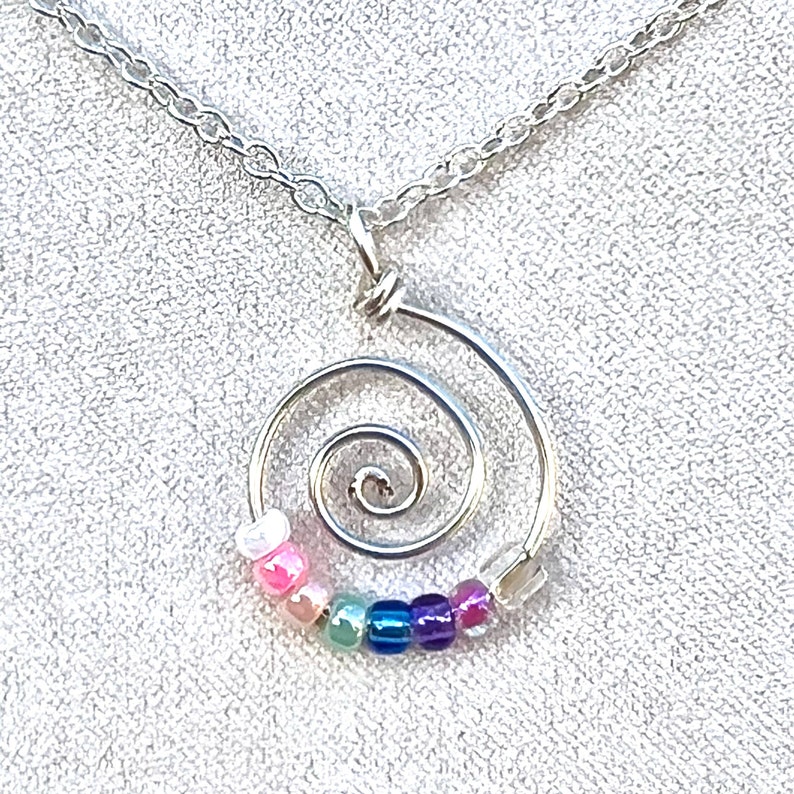 May include: A silver necklace with a spiral pendant. The pendant is decorated with colorful beads in shades of pink, green, blue, and purple.