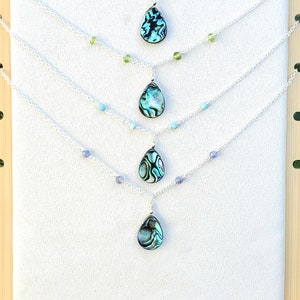May include: Five silver necklaces with abalone shell pendants and various colored beads. The necklaces are displayed on a wooden background.