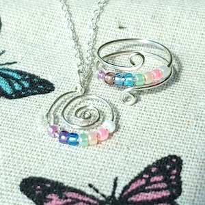 May include: A silver necklace and ring set with a spiral design and colorful beads. The beads are in shades of pink, blue, green, and purple.