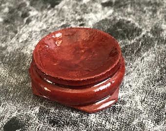 May include: A small, round, wooden display stand with a glossy, dark red finish. The stand has a slightly raised lip around the top edge.