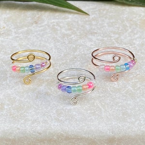 May include: Three adjustable rings with a rainbow of iridescent beads. The rings are made of gold, silver, and rose gold wire.