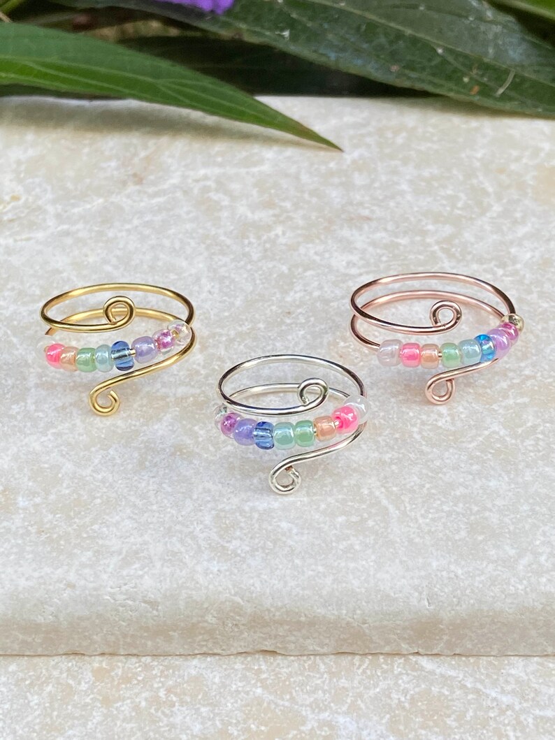 May include: Three adjustable rings with a rainbow of iridescent beads. The rings are made of gold, silver, and rose gold wire.