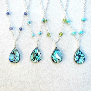 May include: Four silver necklaces with abalone shell pendants and different colored beads. The necklaces feature blue, green, and turquoise beads.