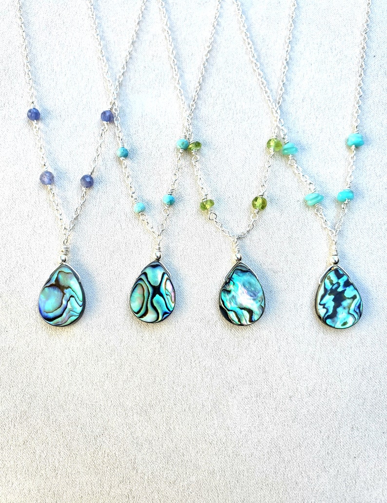 May include: Four silver necklaces with abalone shell pendants and different colored beads. The necklaces feature blue, green, and turquoise beads.