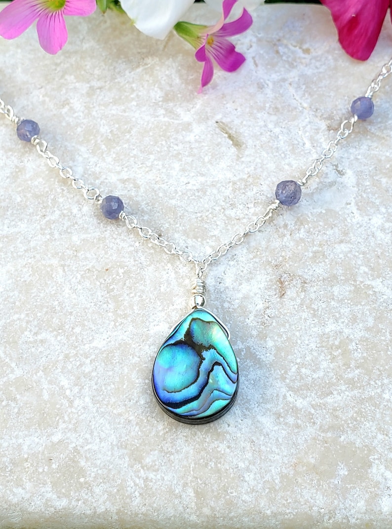 May include: A silver chain necklace with a teardrop-shaped abalone shell pendant and small amethyst beads.