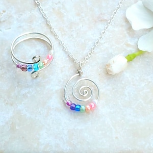 May include: A silver necklace and ring set with a spiral design and colorful beads. The necklace has a delicate chain and the ring is adjustable.