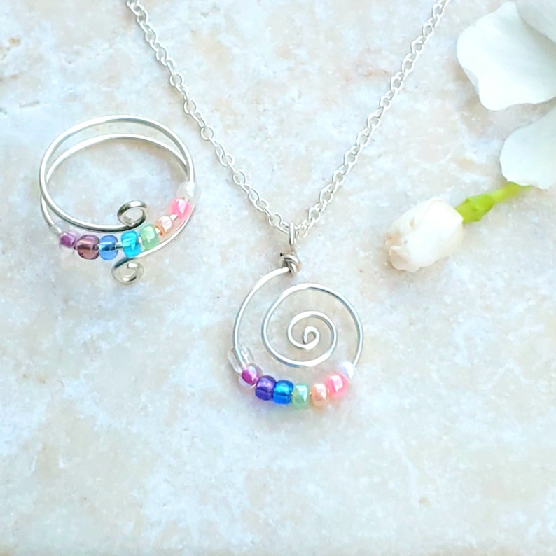 May include: A silver necklace and ring set with a spiral design and colorful beads. The necklace has a delicate chain and the ring is adjustable.