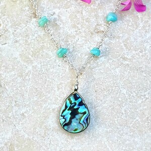 May include: A silver chain necklace with a teardrop-shaped abalone shell pendant and turquoise beads.