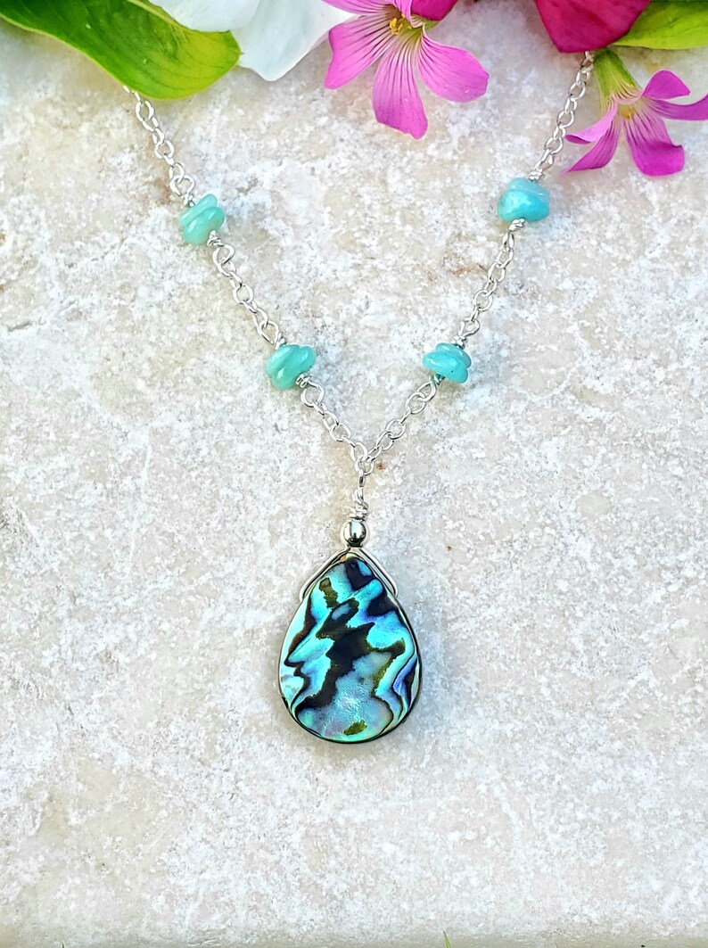 May include: A silver chain necklace with a teardrop-shaped abalone shell pendant and turquoise beads.
