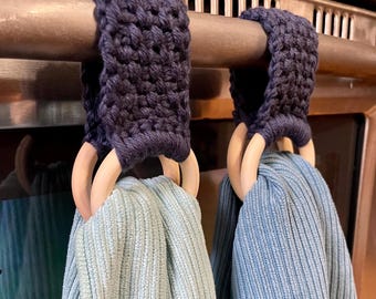 May include: Two blue kitchen towels hanging on a metal rack with wooden rings. The towels are ribbed and the rings are natural wood. The rack is attached to a brown cabinet.