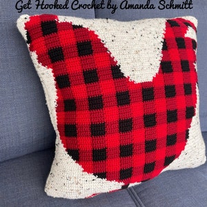 May include: A red and black plaid crocheted pillow in the shape of a bird. The pillow is sitting on a blue couch. The text "Get Hooked Crochet by Amanda Schmitt" is visible at the top of the image.
