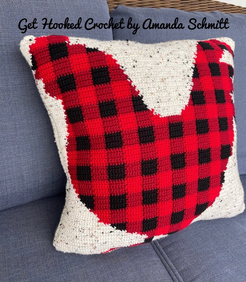 May include: A red and black plaid crocheted pillow in the shape of a bird. The pillow is sitting on a blue couch. The text "Get Hooked Crochet by Amanda Schmitt" is visible at the top of the image.