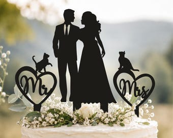 May include: A black silhouette cake topper featuring a couple standing together, flanked by two heart-shaped accents. The left heart contains the text Mr with a cat on top, and the right heart contains the text Mrs with a cat on top.