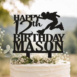 May include: A black cake topper featuring the text HAPPY 12th BIRTHDAY MASON with a silhouette of a person roller skating. The topper has two prongs at the base for insertion into a cake, and the design is cut from a single piece of material.