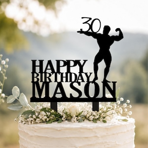 Pode incluir: Um topo de bolo preto com o texto "HAPPY BIRTHDAY MASON" em fonte negrito, encimado pela silhueta de uma figura musculosa posando e o número "30". O topo possui duas hastes na base para inserção no bolo.