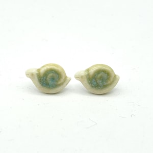 May include: Two small ceramic snail figurines. Each snail has a cream-colored body with a swirled, green and blue shell. The snails are positioned side-by-side against a white background. These miniature snails could be used as decorative accents.