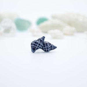 May include: A small, blue seashell with a textured surface. The seashell is made of ceramic and has a delicate, intricate design.