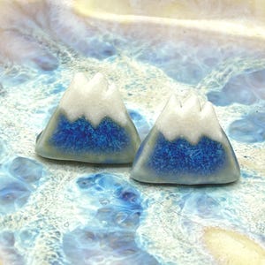 May include: A pair of ceramic earrings shaped like mountains with white peaks and a blue base.