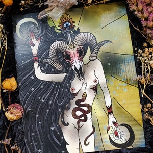 May include: A digital illustration of a woman with a ram skull for a head. She has a snake wrapped around her torso and is holding a crescent moon in each hand. The background is a yellow and gold color with stars.