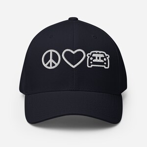 Könnte beinhalten: Eine marineblaue Baseballkappe mit einem weißen gestickten Peace-Zeichen, einem Herzen und einem Auto. Die Kappe hat einen gebogenen Schirm und eine strukturierte Krone.