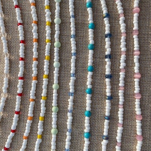 May include: A collection of white beaded necklaces with various colored beads, including red, orange, yellow, green, blue, and pink.