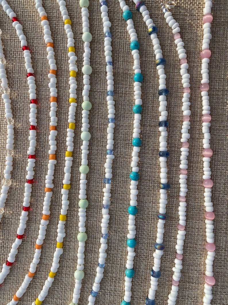 May include: A collection of white beaded necklaces with various colored beads, including red, orange, yellow, green, blue, and pink.