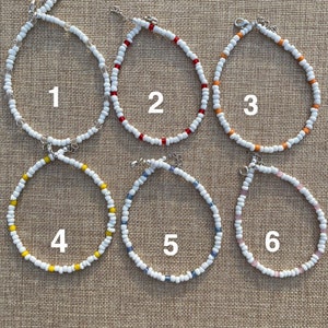 May include: Six beaded necklaces with white beads and different colored accent beads. The necklaces are numbered 1 through 6.