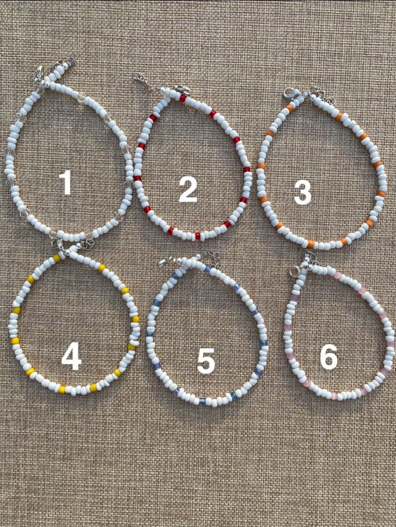 May include: Six beaded necklaces with white beads and different colored accent beads. The necklaces are numbered 1 through 6.