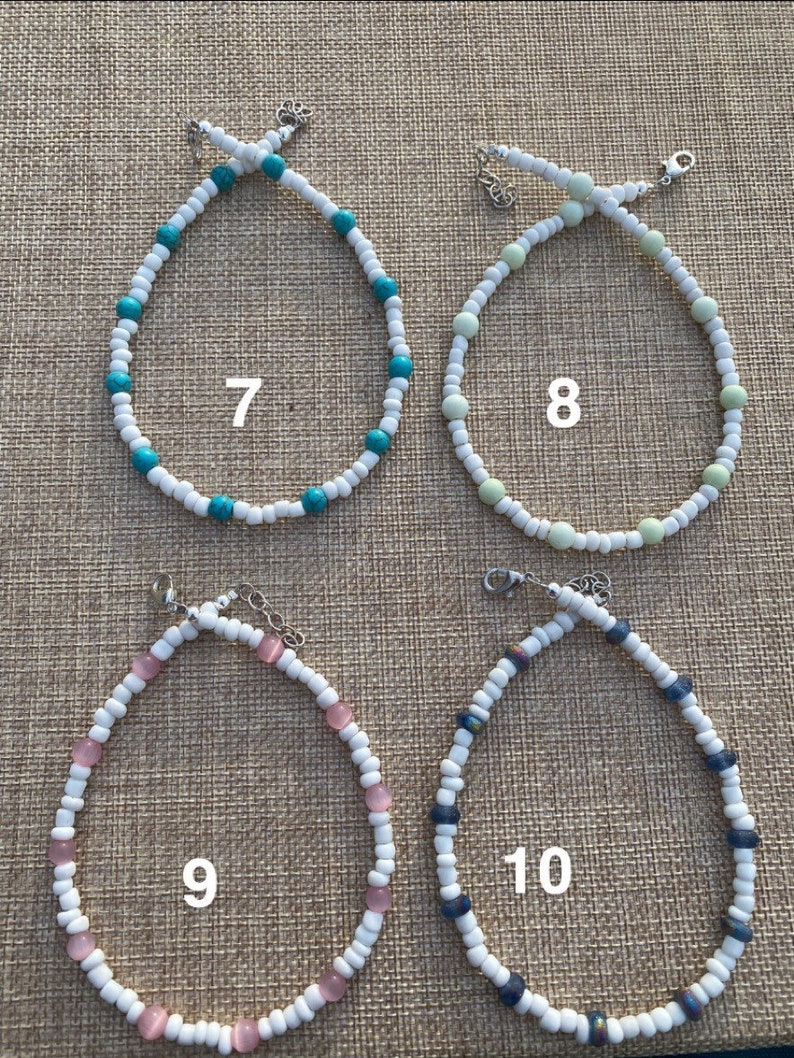 May include: Four beaded necklaces with white beads and different colored accent beads. The necklaces are numbered 7, 8, 9, and 10.