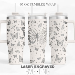 Puede incluir: Un vaso blanco de 40 onzas con un diseño de mariposa y flores plateadas. El vaso tiene un asa y una tapa con una pajita. El texto "LASER ENGRAVED SVG. PNG" está en la parte inferior de la imagen.