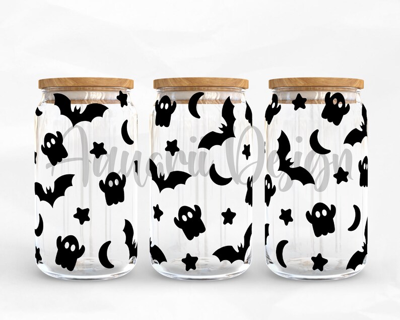 May include: Three clear glass jars with wooden lids, each decorated with a black and white Halloween themed pattern of bats, ghosts, stars, and moons.