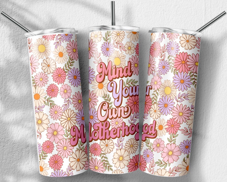 May include: Three stainless steel tumblers with a white background and a floral pattern in shades of pink, purple, and yellow. The middle tumbler has the text "Mind Your Own Motherhood" in pink and orange letters.