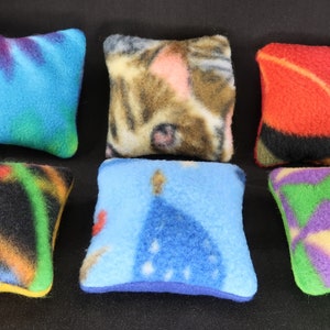 Könnte beinhalten: Sechs bunte quadratische Kissen mit verschiedenen Mustern. Die Kissen sind aus weichem Fleece-Stoff gefertigt und eignen sich perfekt, um jedem Raum einen Hauch von Farbe und Gemütlichkeit zu verleihen.