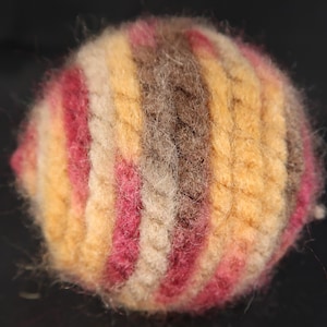 May include: A round ball of yarn with stripes of pink, beige, brown, and yellow.